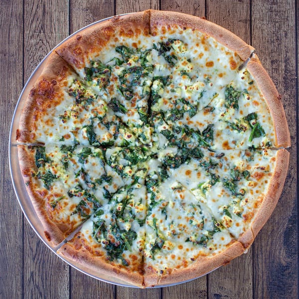 A whole Fotia Greek Taverna spinach and feta pizza, sliced, on a metal tray.