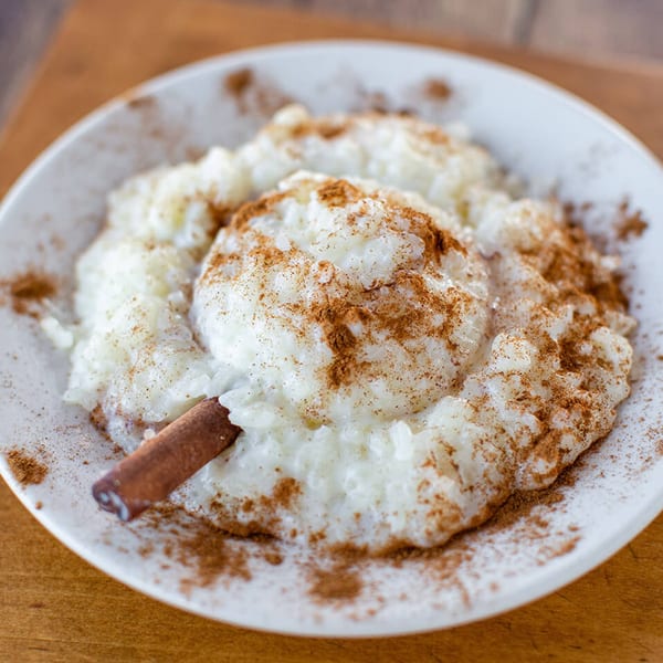 Creamy Greek rice pudding (rizogalo) with cinnamon powder and a cinnamon stick on a white plate.