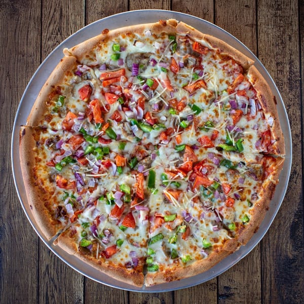 Overhead view of a Fotia Greek Taverna pizza with tomatoes, onions, peppers, and cheese.