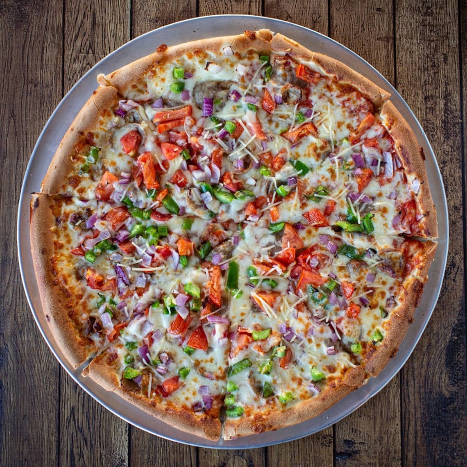 Overhead view of a Fotia Greek Taverna pizza with tomatoes, onions, peppers, and cheese.