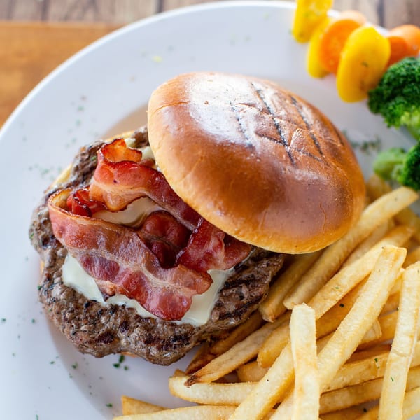 Bacon cheeseburger with fries, broccoli, and bell pepper skewers on a white plate.