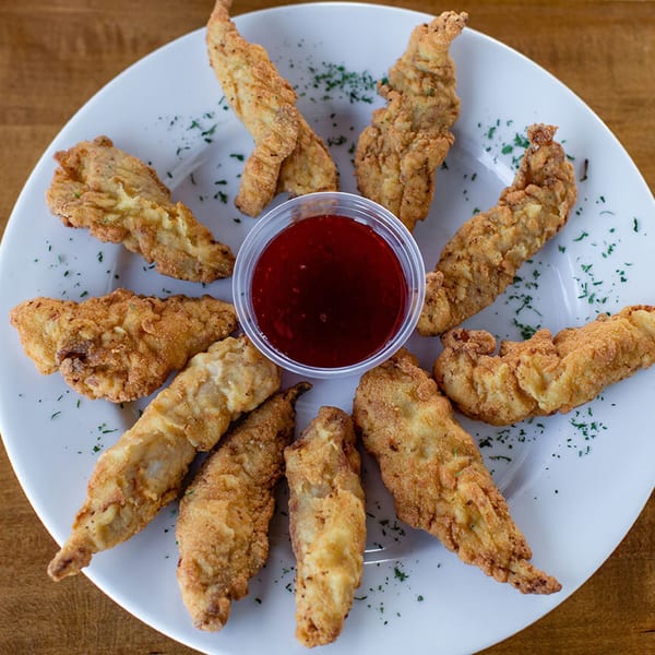 Golden-brown fried chicken tenders arranged in a circle around a cup of red dipping sauce.