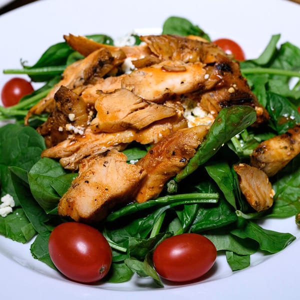 Fotia Greek Taverna's grilled chicken salad with spinach, feta, and cherry tomatoes on a white plate.